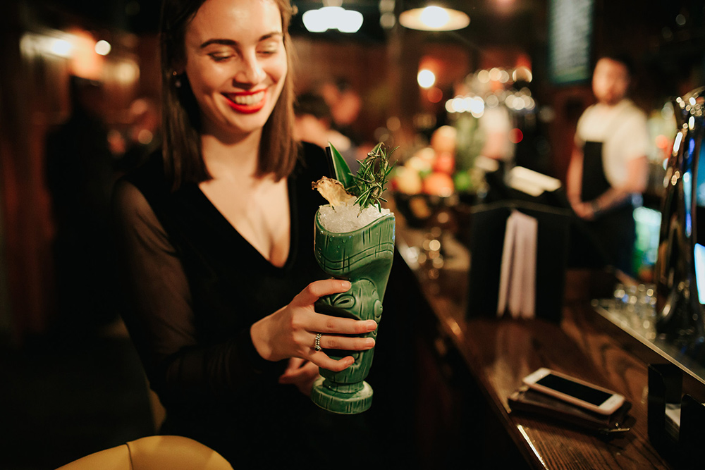 Female patron holding tiki-themed cocktail in Chambers Cocktail Company