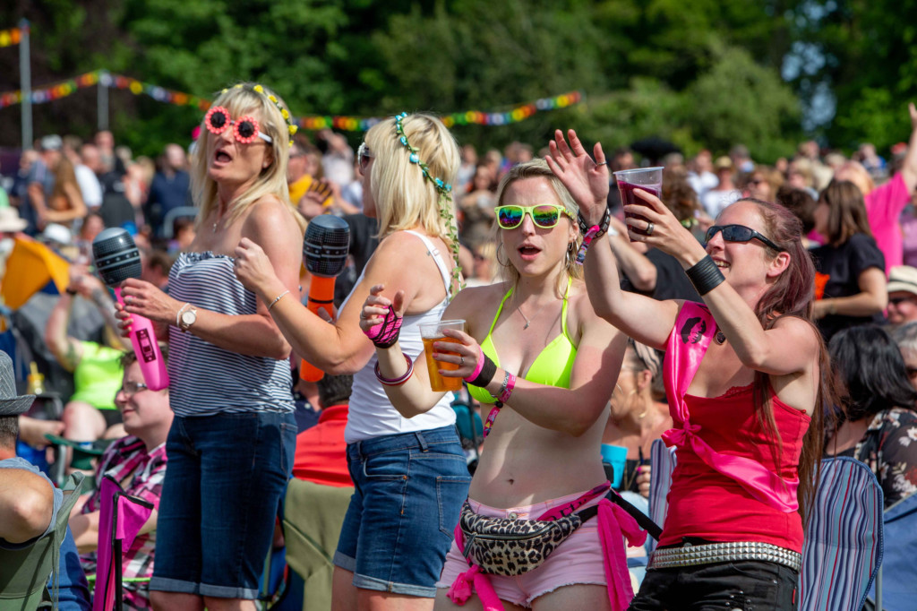 Four women at Lets Rock are dancing in neon clothes, holding drinks and inflatable microphones